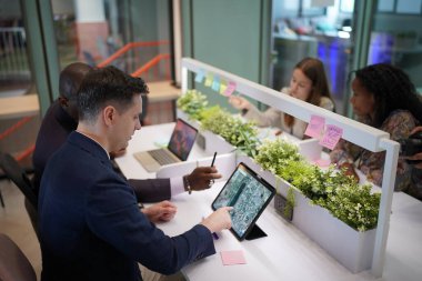 Genç iş adamları ve meslektaşlarının toplantıda laptopta ve dokunmatik kağıtları tartışırken görüntüsü