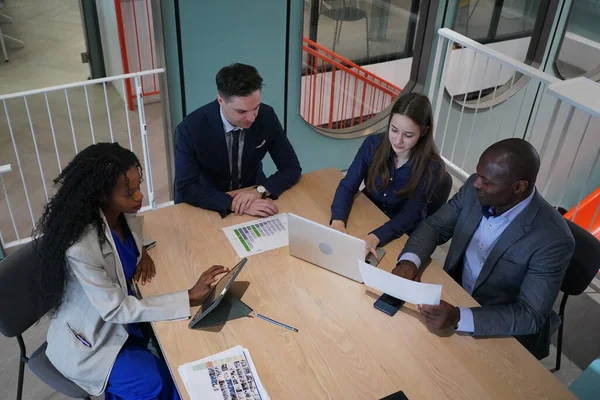 Genç iş adamları ve meslektaşlarının toplantıda laptopta ve dokunmatik kağıtları tartışırken görüntüsü