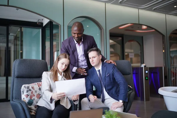 Genç iş adamları ve meslektaşlarının toplantıda laptopta ve dokunmatik kağıtları tartışırken görüntüsü