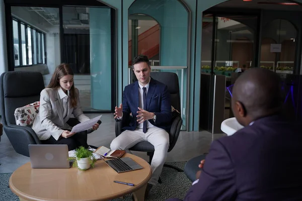 Genç iş adamları ve meslektaşlarının toplantıda laptopta ve dokunmatik kağıtları tartışırken görüntüsü
