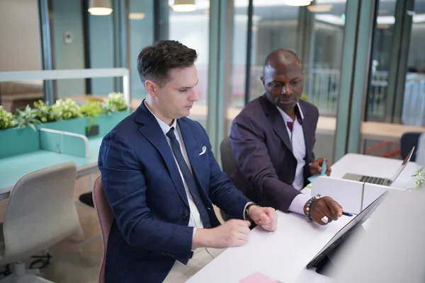 Genç iş adamları ve meslektaşlarının toplantıda laptopta ve dokunmatik kağıtları tartışırken görüntüsü