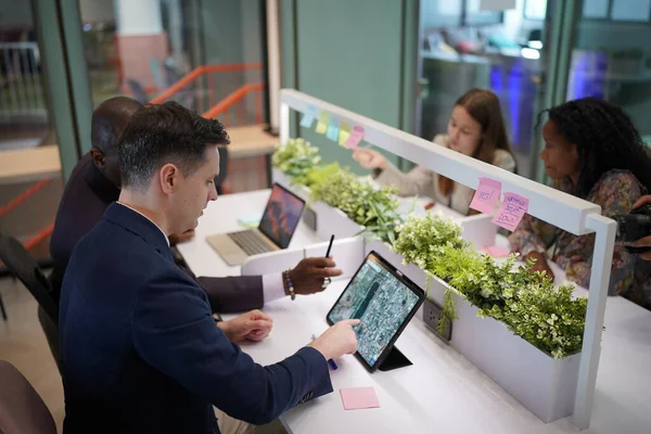 Genç iş adamları ve meslektaşlarının toplantıda laptopta ve dokunmatik kağıtları tartışırken görüntüsü