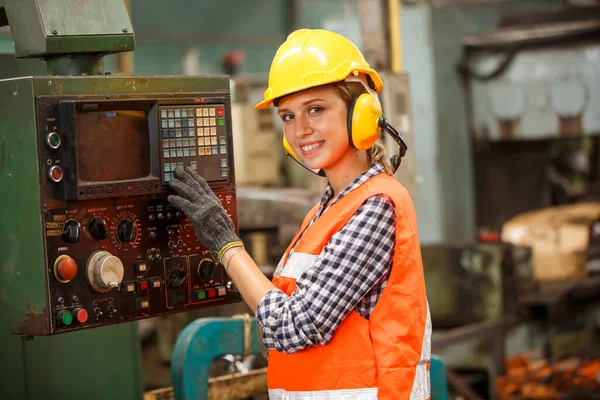 Kasklı ve koruyucu eldivenli kadın işçi fabrikada çalışıyor.