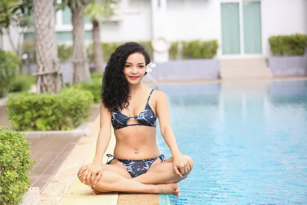 Attractive young woman in sexy bikini at poolside in the outdoor swimming pool, mixed race long hair woman.