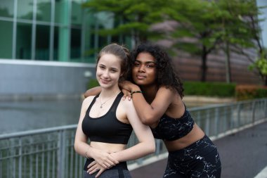 Young sporty attractive woman practicing yoga, doing yoga exercise with friend, yoga pose, working out, wearing sportswear, pants and top, outdoor full length