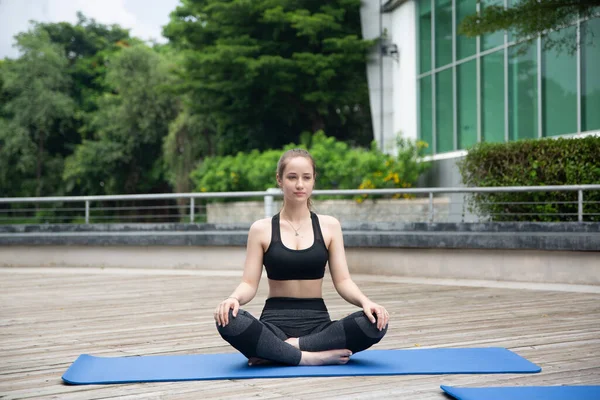 Young sporty attractive woman practicing yoga, doing yoga exercise with friend, yoga pose, working out, wearing sportswear, pants and top, outdoor full length
