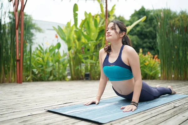 Young sporty attractive woman practicing yoga, doing yoga exercise with friend, yoga pose, working out, wearing sportswear, pants and top, outdoor full length
