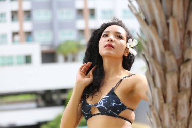 Attractive young woman in sexy bikini at poolside in the outdoor swimming pool, mixed race long hair woman.