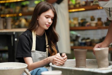 Çömlekçide oturan önlüklü güzel zanaatkar kadının yakın çekimi.