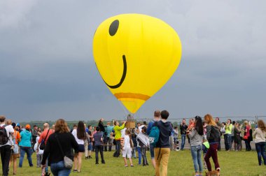Üzerinde gülen surat sembolü olan balon, sahada bir sürü insanla birlikte uçuyor.