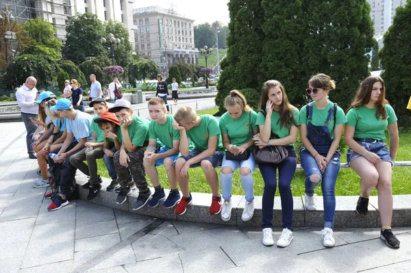 Group of teenagers in green T-shirts sitting on a bench in a park. Street action protest against human trafficking in the world — Stock Photo, Image