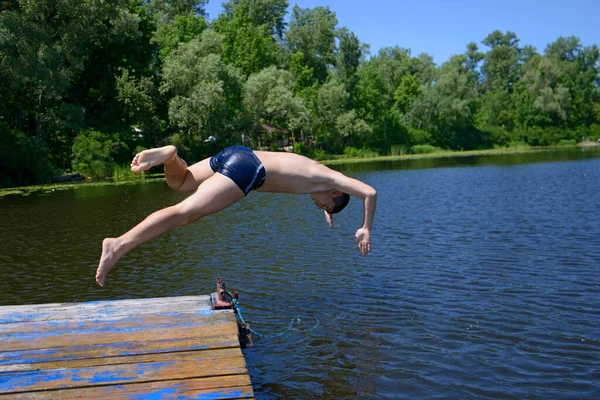 Küçük çocuk tahta iskeleden nehre balıklama atlıyor. 25 Mayıs 2019. Kiev, Ukrayna