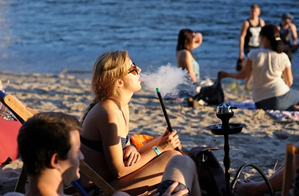 Chica sentada en una playa y fumando una cachimba, gente sobre un fondo — Foto de Stock