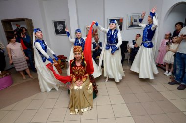 Kırım Tatar geleneksel nikahı: nedimeler bir gelini damat ile buluşmaya hazırlarken kırmızı örtüsünü örterler. Kırım Tatar Kültürü Günleri. 27 Şubat 2019. Kiev, Ukrayna