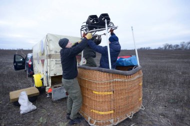 Balon şişirme hazırlıkları: erkekler gaz ocağını arka planda ekipman bulunan sepetin, arabanın ve römorkun üstüne koyuyorlar. 12 Ocak 2020. Kiev, Ukrayna