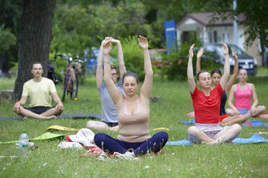 Bir grup genç erkek ve kadın şehir parkının çimlerinde yoga egzersizi yapıyorlar. Temmuz 04, 2020. Kyiv, Ukrayna