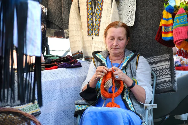 El yapımı giysiler ve örgü örerek tezgahta oturan gülümseyen yaşlı bir kadın sokak satıcısı. Andreevsky iniyor. 12 Eylül 2020. Kyiv, Ukrayna