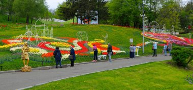 People walking in the city park and looking at bright tulips planted on a lawn. Opening the Festival of tulips Around the World , Singing Field park. April 27, 2018. Kiev, Ukraine