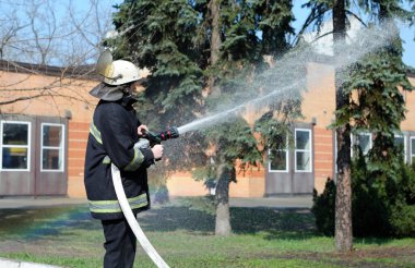Fireman in protective costume watering plant territory with syringe - Rescue team training of firefighting. April 5, 2019. Forestry of Sviatoshyn district, Kievskaya oblast, Ukraine