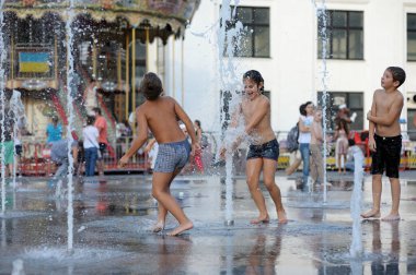 Strong heat in the city: laughing children playing with fountain water jets at the square. June 5, 2018. Kyiv, Ukraine