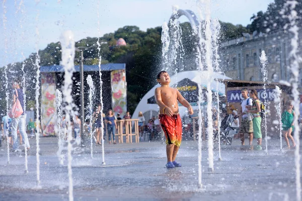 Şehirde güçlü bir sıcaklık var: Meydanda fıskiyelerle oynayan gülen küçük çocuk. 5 Haziran 2018. Kiev, Ukrayna