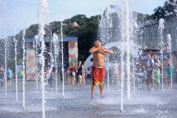 Şehirde güçlü bir sıcaklık var: Meydanda fıskiyelerle oynayan gülen küçük çocuk. 5 Haziran 2018. Kiev, Ukrayna