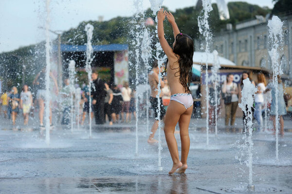 Strong heat in the city: laughing little girl playing with fountain water jets at the square. June 5, 2018. Kiev, Ukraine
