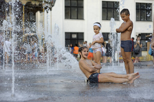Strong heat in the city: laughing children playing with fountain water jets at the square. June 5, 2018. Kyiv, Ukraine