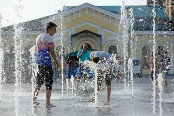 Şehirde güçlü bir sıcaklık var: Meydanda fıskiyelerle oynayan gülen genç adam. 5 Haziran 2018. Kyiv, Ukrayna