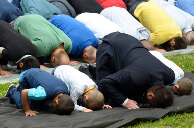 Bir grup Müslüman, çimenlerde diz çöküp dua ediyor.