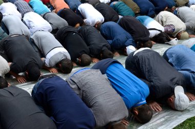 Bir grup Müslüman, çimenlerde diz çöküp dua ediyor.