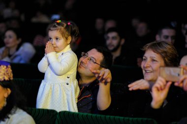 Kırım Tatar kızı konser sırasında sahnede şaşkınlıkla bakıyor, yetişkinler koltuklarda alkışlıyor. Nowruz 'u kutluyoruz. 24 Aralık 2017. Kyiv, Ukrayna