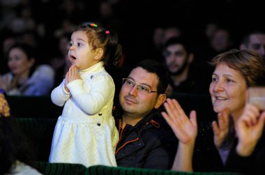 Kırım Tatar kızı konser sırasında sahnede şaşkınlıkla bakıyor, yetişkinler koltuklarda alkışlıyor. Nowruz 'u kutluyoruz. 24 Aralık 2017. Kyiv, Ukrayna