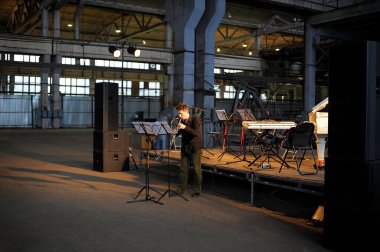 Bir fabrikanın eski üretim salonunda flüt çalan yalnız bir müzisyen, arkasında müzik aletleri olan boş bir sahne. GogolFest Festivali. 17 Eylül 2012. Kyiv Ukrayna