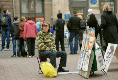 Man street painter sitting on a folding chair waiting for customers, crowd of people walking around. October 21, 2012. Kyiv, Ukraine