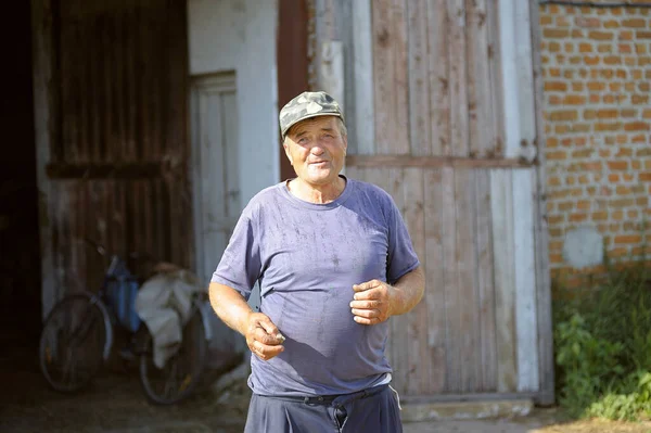 An old man farm worker standing in front of a stable, rural farm. August 30, 2019. Mena, Ukraine.