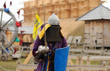 Reenactor man dressed in armor of an Old Rus footman reconstructing sword fight, wooden fortress on a background. Kyiv, Ukraine