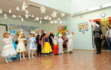 Children in carnival costumes performing in the kindergarten during New Year eve party, woman host helping them. December 29, 2013. Kyiv, Ukraine