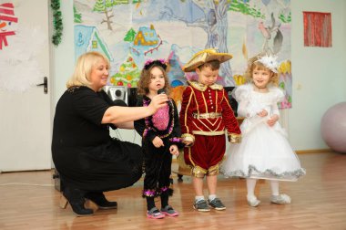 Children in carnival costumes performing in the kindergarten during New Year eve party, woman host helping them. December 29, 2013. Kyiv, Ukraine