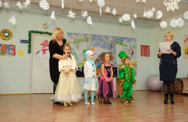 Children in carnival costumes performing in the kindergarten during New Year eve party, woman host helping them. December 29, 2013. Kyiv, Ukraine
