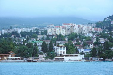 Resort town Gurzuf, buildings beach mountains plunged in a fog, cloudy sky, view from the sea. Southern coast of the Black Sea, Crimea.