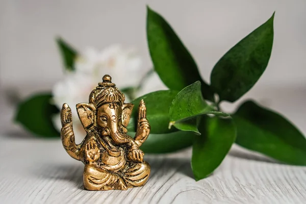 Beyaz çiçekler ve arka planda yeşil yaprakla süslenmiş Bronz Ganapathi Ganesha Idol