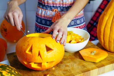 Cadılar Bayramı balkabağı kesme işlemi, Jack-o-fener yapma süreci. Bıçaklı kadın eller, mutfak masasında kalan balkabağı. Seçici odak ve bokeh.