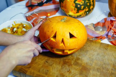 Cadılar Bayramı balkabağı kesme işlemi, Jack-o-fener yapma süreci. Bıçaklı kadın eller, mutfak masasında kalan balkabağı. Seçici odak ve bokeh.