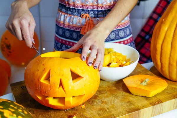 Cadılar Bayramı balkabağı kesme işlemi, Jack-o-fener yapma süreci. Bıçaklı kadın eller, mutfak masasında kalan balkabağı. Seçici odak ve bokeh.
