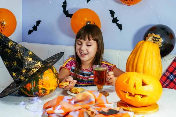Małe, kaukaskie dziecko w kapeluszu czarownicy bawiące się podczas robienia dyń Halloween ręcznie. Jest w salonie.. — Zdjęcie stockowe