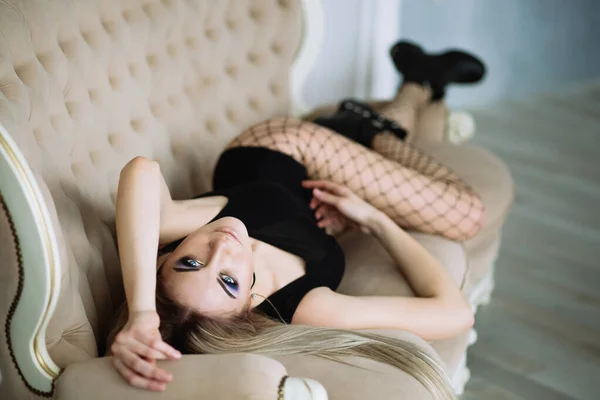 身穿黑色紧身衣、长裤软管和粗糙皮靴的年轻貌美女子站在沙发上 — 图库照片