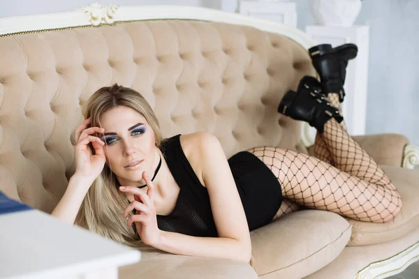 Junge schöne Frau im schwarzen Body mit Strumpfhose und groben Lederstiefeln posiert auf dem Sofa — Stockfoto