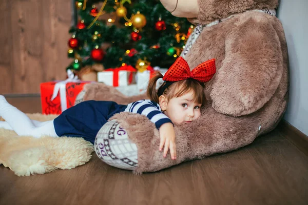 Küçük bir kız Noel Baba 'nın Noel' de verdiği oyuncak ayıyla yatmaktan zevk alıyor. Yeni yıl dekorasyonu — Stok fotoğraf