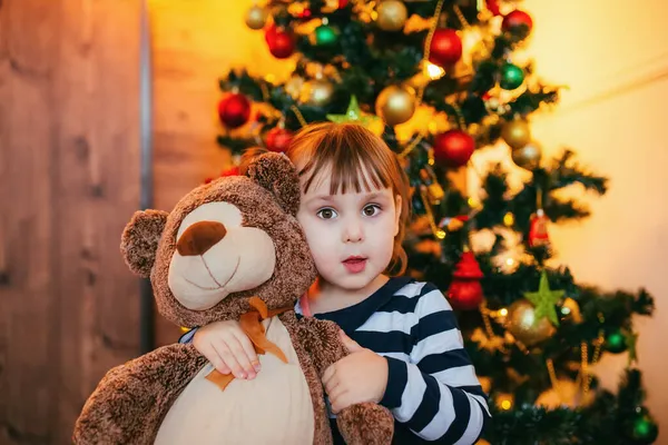 Küçük bir kız, Noel Baba 'nın Noel için verdiği yeni oyuncak ayısının tadını çıkarıyor. Yeni yıl dekorasyonu — Stok fotoğraf
